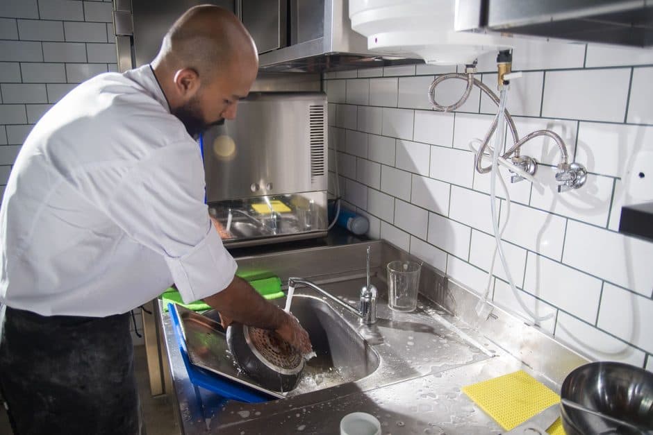 A frying pan being washed under running water in a sink.