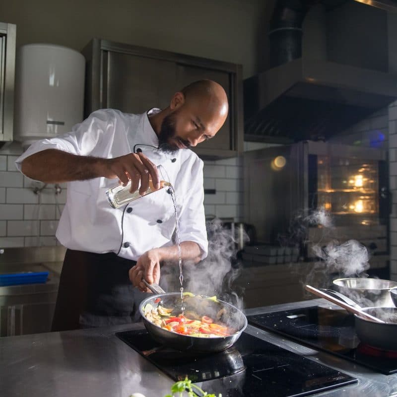 A chef cooking in a heavy stainless pan. Illustrative stock photograph, not a photograph of a specific Demeyere pan.