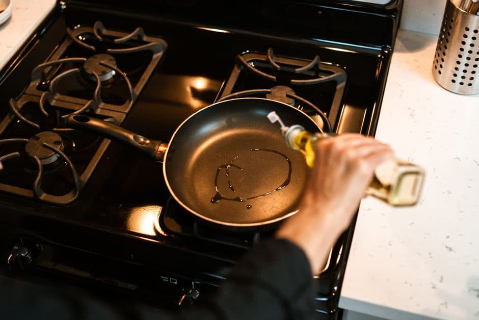 Oil being poured into a dark nonstick frying pan.