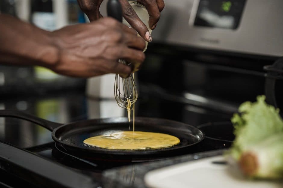 Eggs being poured into a rounded stainless steel pan.
