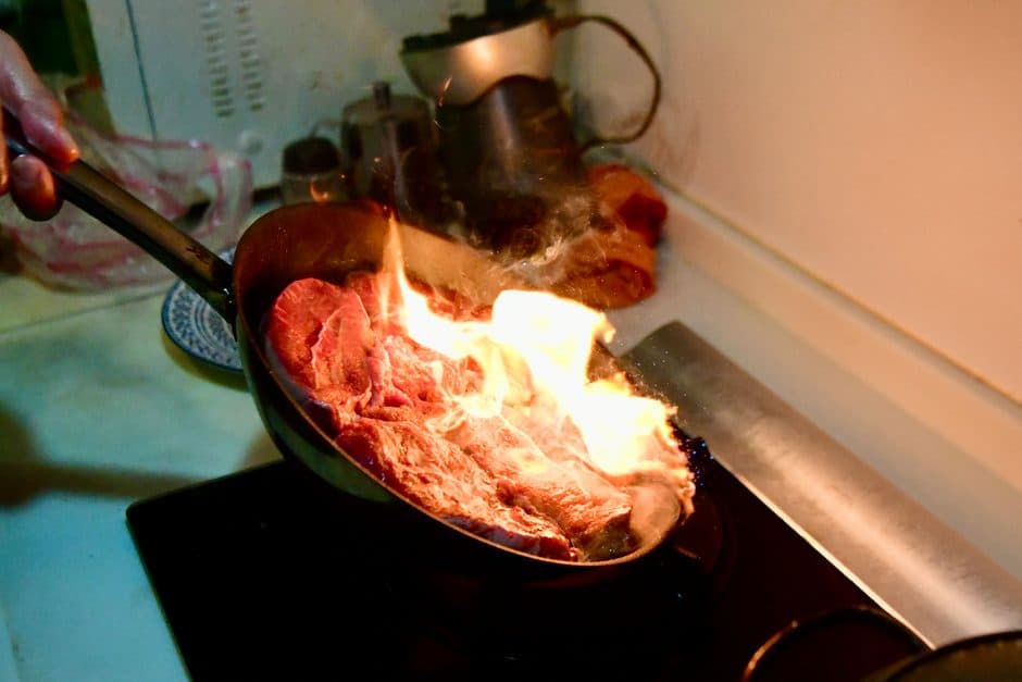 A steak searing in a stainless steel pan.