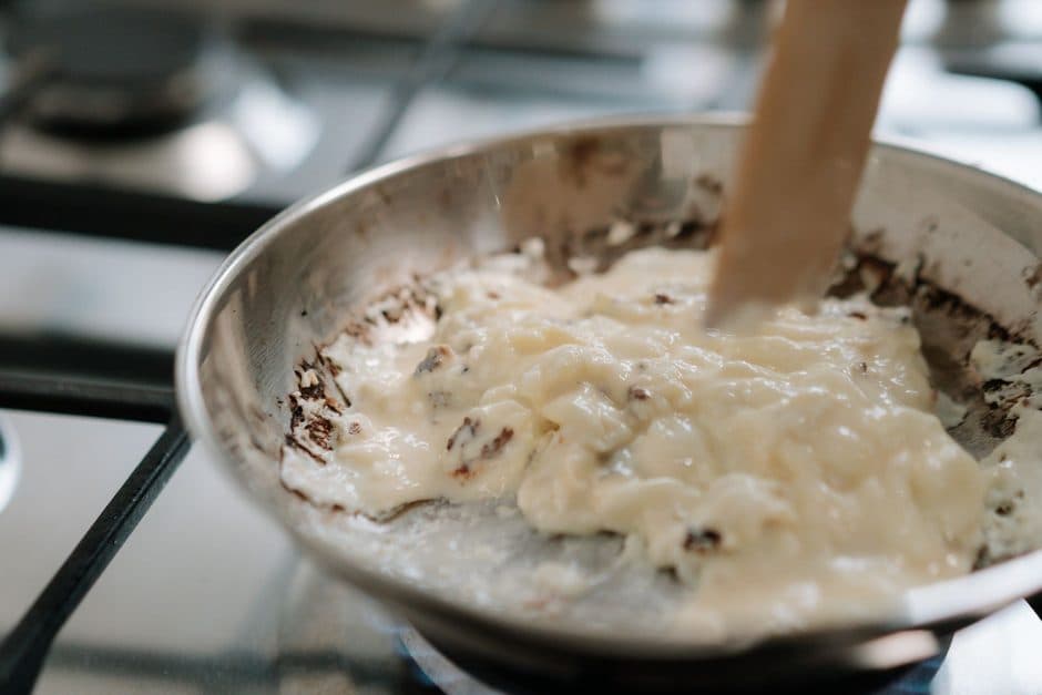 A creamy sauce being whisked in a stainless steel bowl.